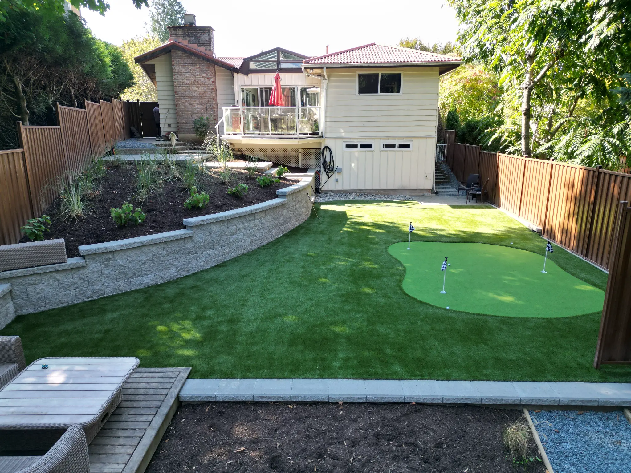 Wide completed backyard view showing the putting green and terraced planting bed