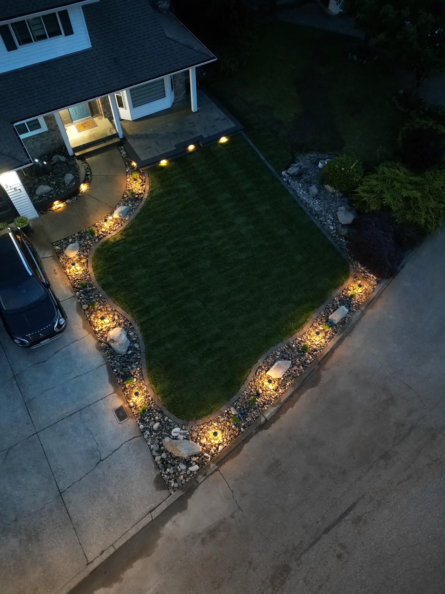 Front yard with landscape lighting, rock borders, and manicured lawn at dusk