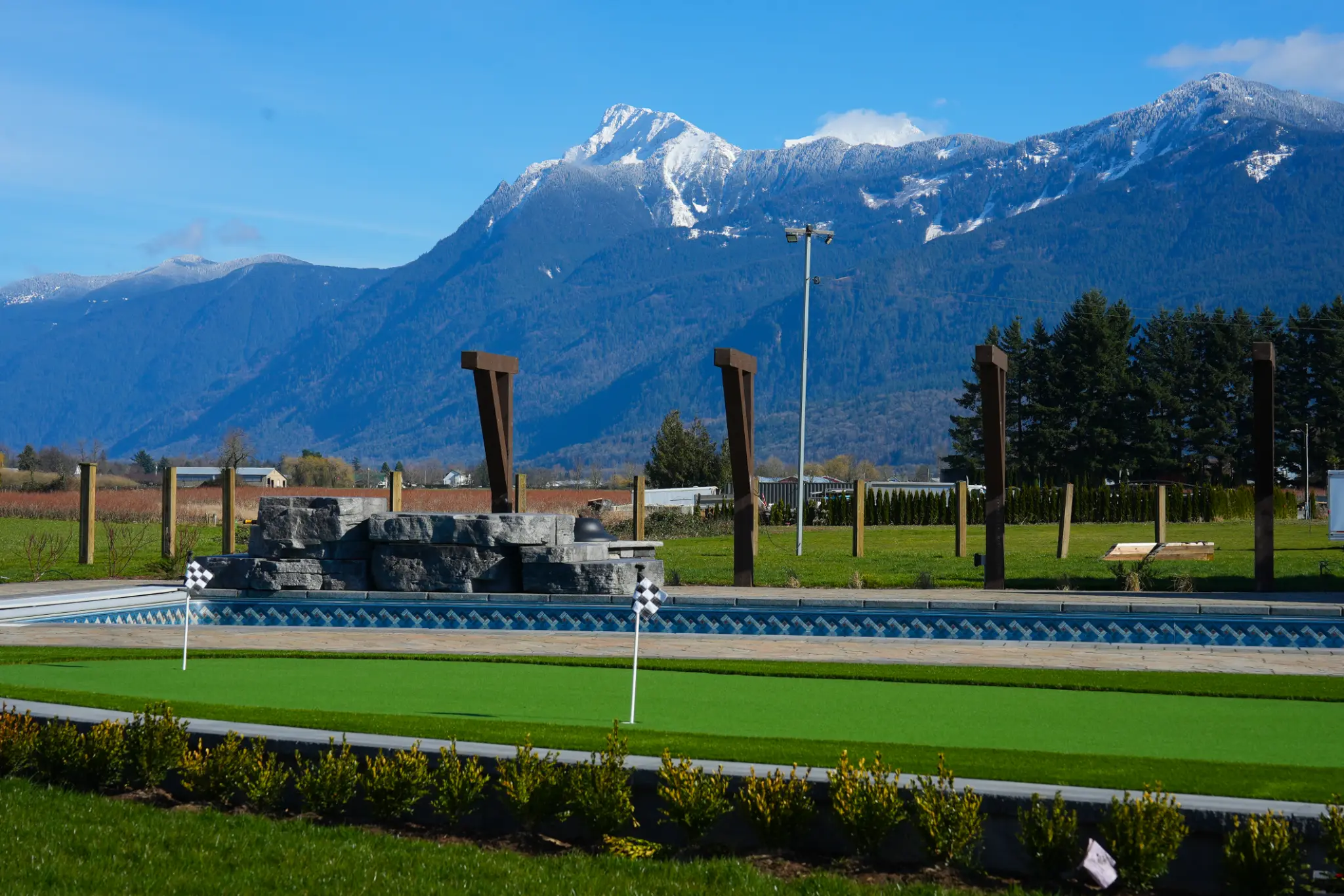 Completed Fraser Valley backyard with a pool, putting green, landscaping, and mountain views