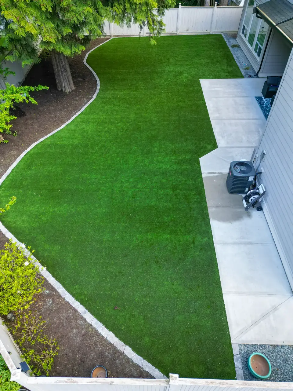 Completed landscape construction with artificial turf, concrete patio, and finished garden beds