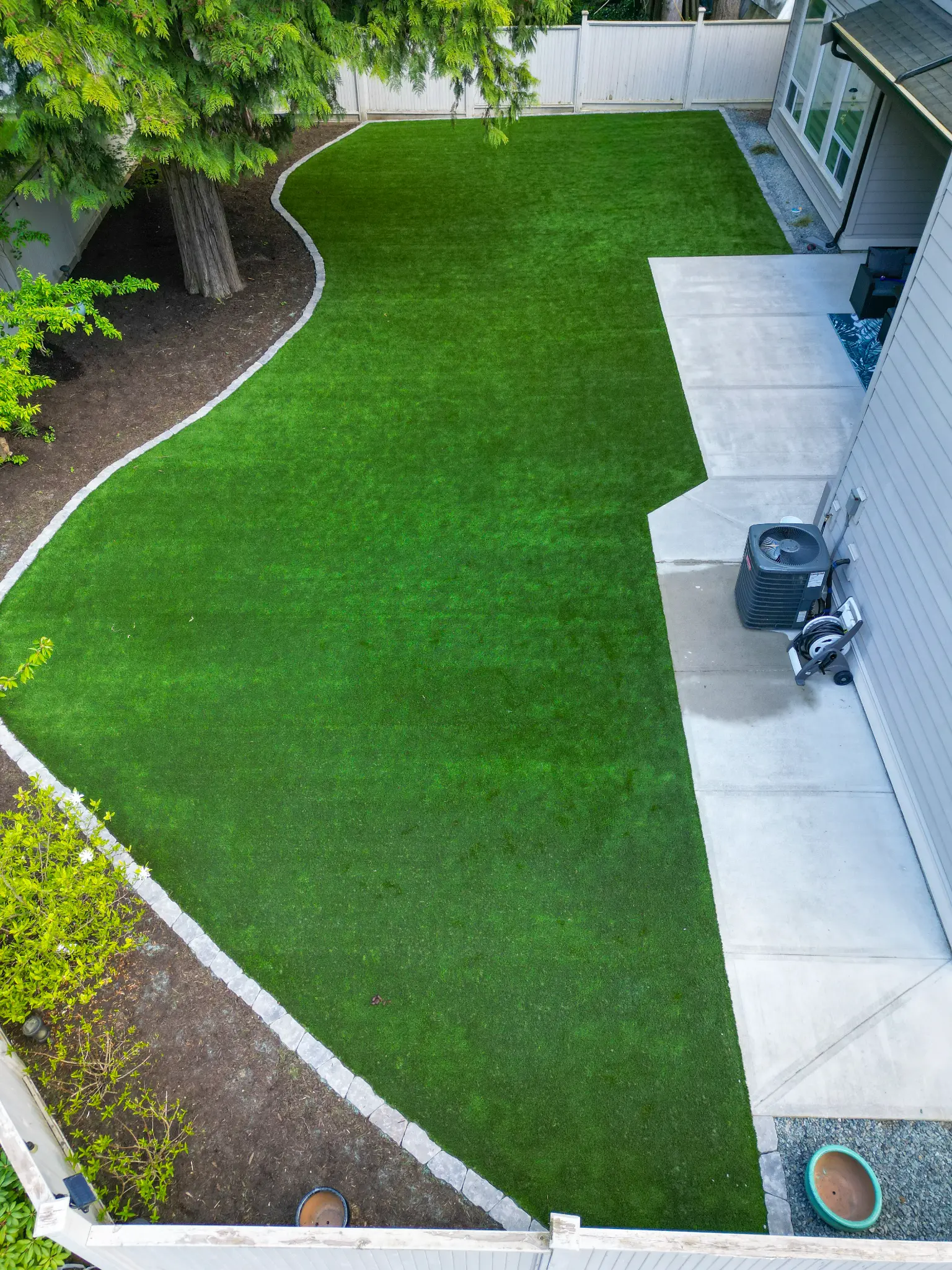 Completed landscape construction with artificial turf, concrete patio, and finished garden beds