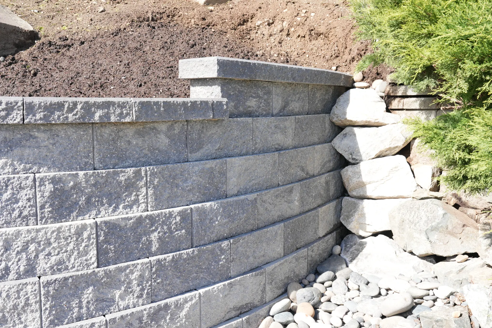 Wide view of curved retaining wall with block construction and river rock